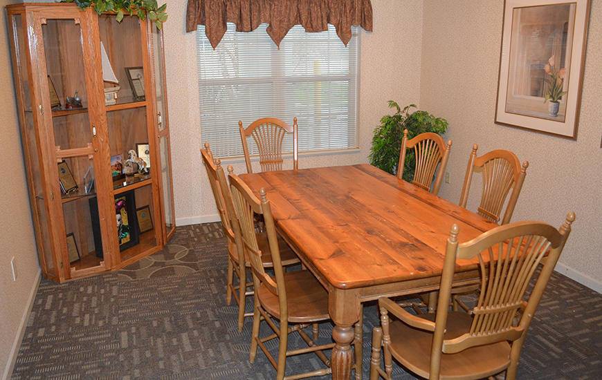 A cozy dining room featuring a wooden table and chairs, a bookshelf, and a window adorned with curtains.