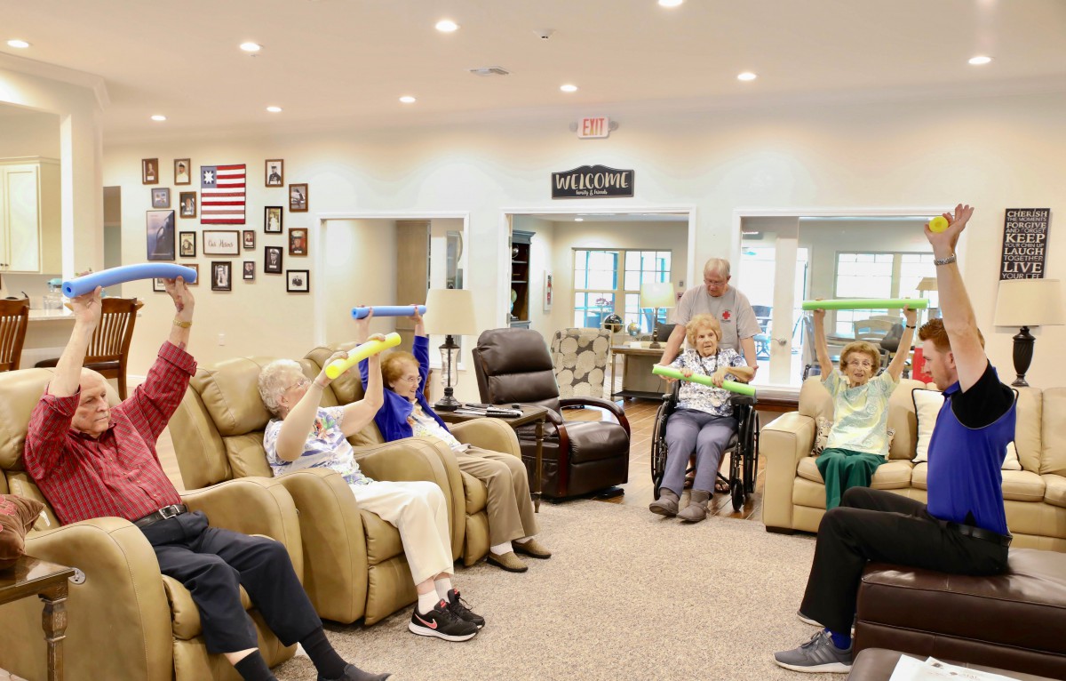 A group of seniors participating in a seated exercise session in a community room.