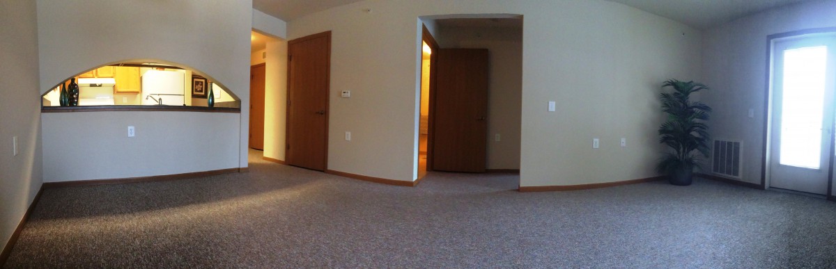 An empty carpeted room with wooden doors and neutral walls.