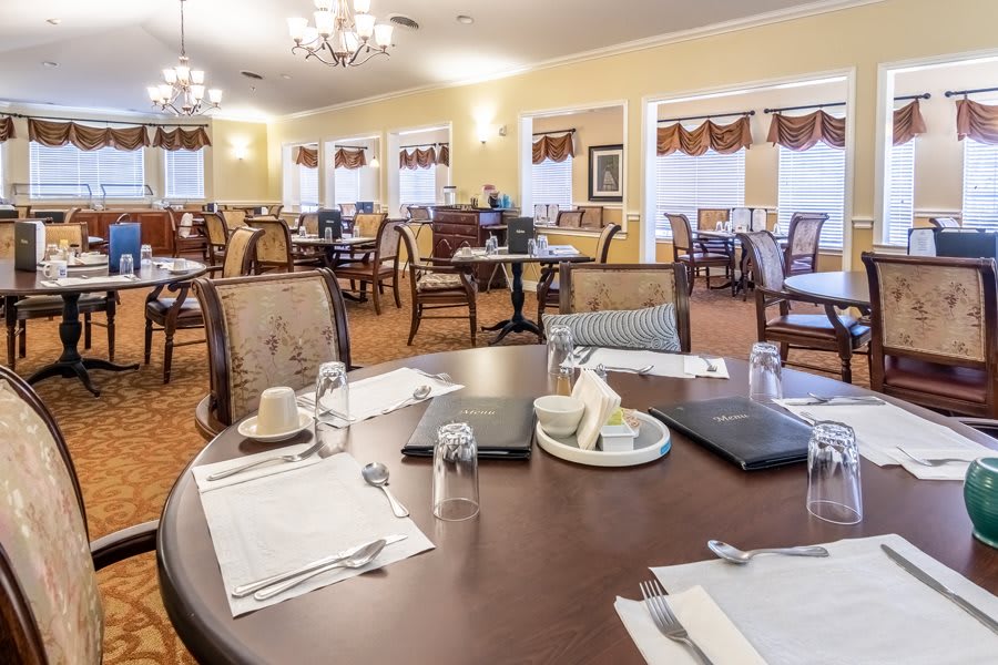An elegant dining room with neatly set tables and comfortable chairs, featuring chandeliers and a warm ambiance.
