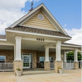 A building with a peaked roof and columns stands prominently, featuring a welcoming entrance.