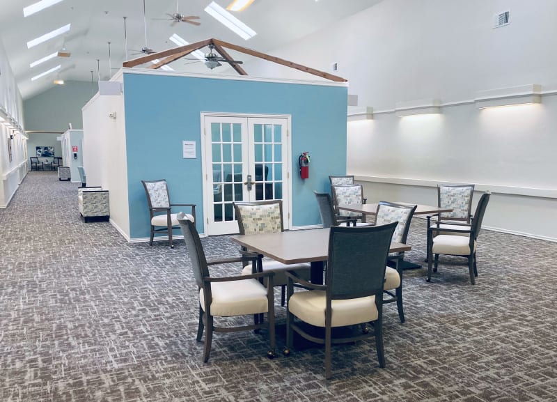 A spacious dining area with several tables and chairs, featuring a blue accent wall and carpeted flooring.