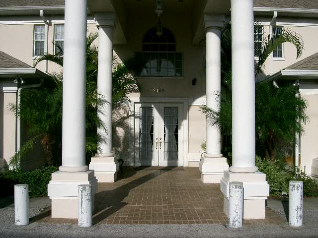 A symmetrical building entrance featuring tall white columns and lush greenery.