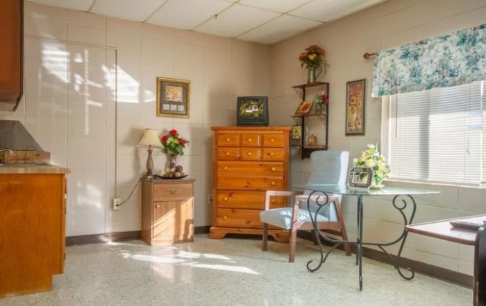 A cozy room featuring a wooden dresser, a blue chair, and various decorative elements including framed pictures and plants.