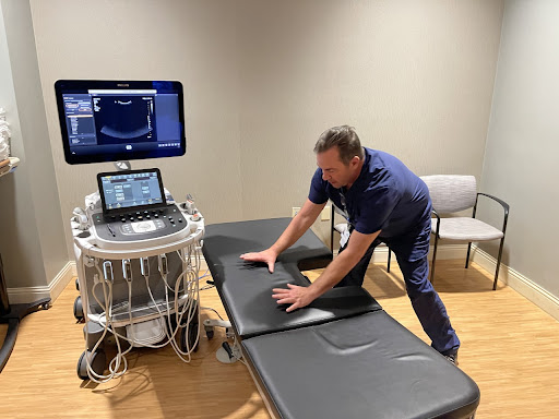 A healthcare professional prepares an ultrasound machine in a medical examination room.