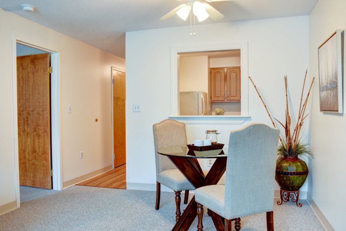 A cozy dining area with a small table and chairs adjacent to an open kitchen in an apartment.