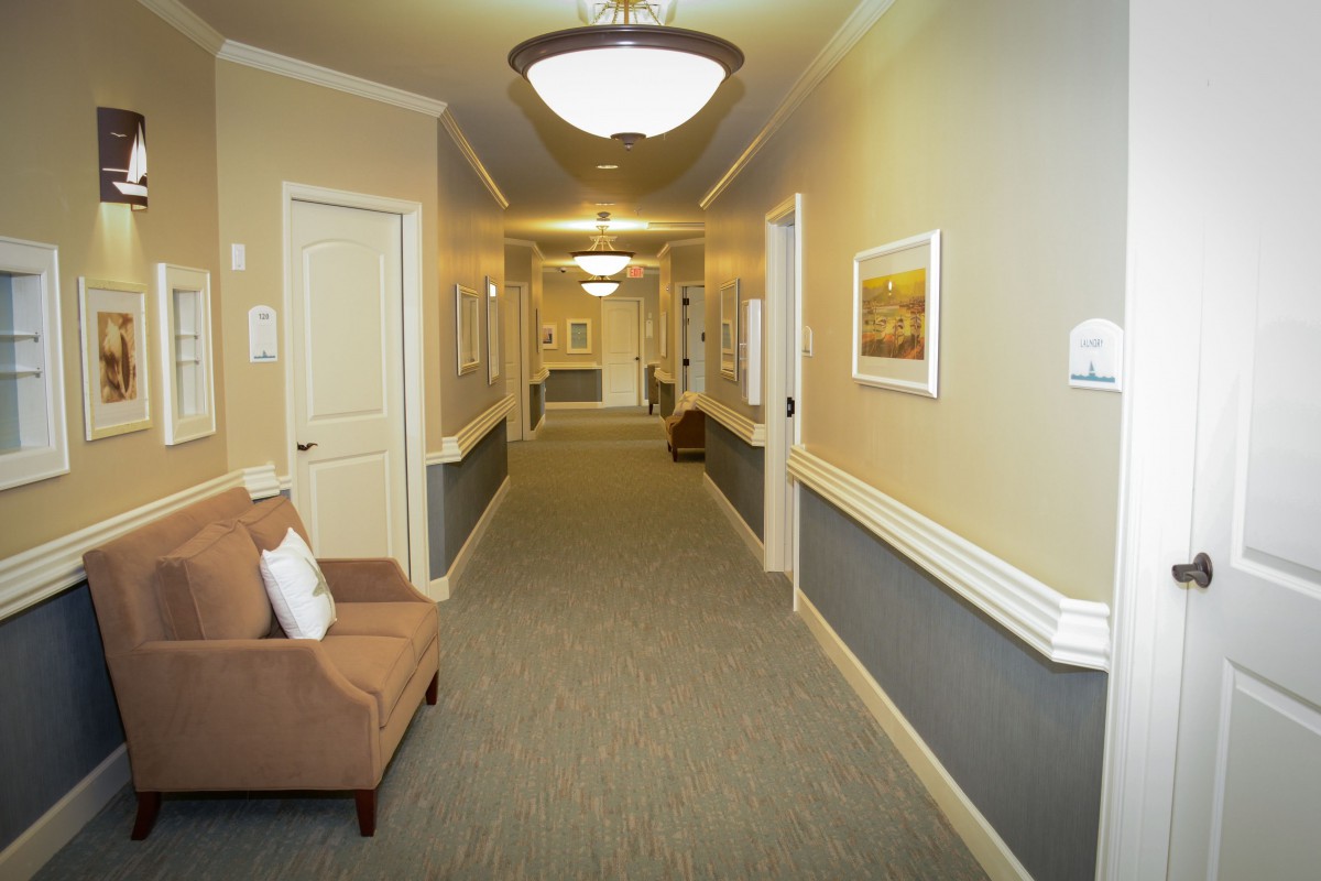 A well-lit hallway with carpeted floor, featuring chairs and artwork on the walls.
