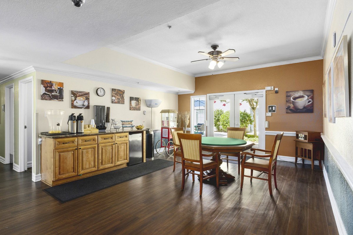 A cozy room with a coffee station and a round dining table surrounded by chairs, featuring wood flooring and large windows letting in natural light.