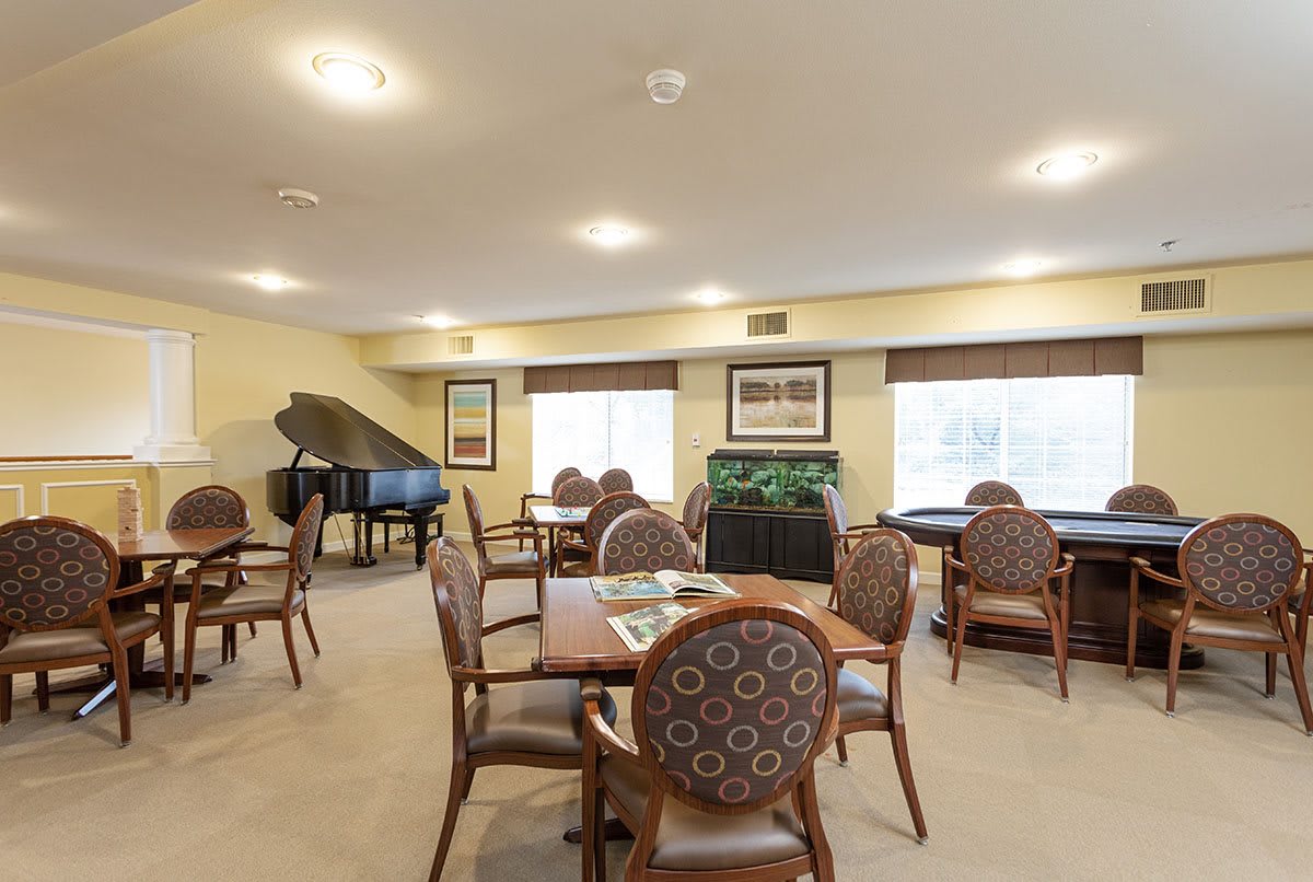 A cozy dining room with tables, chairs, and a grand piano.