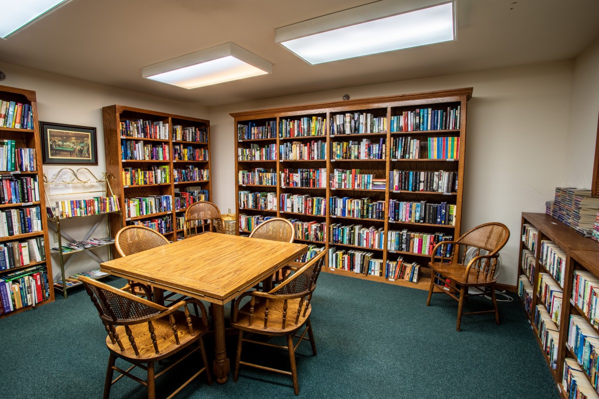 A cozy library reading room with wooden bookshelves filled with books and a table surrounded by chairs.