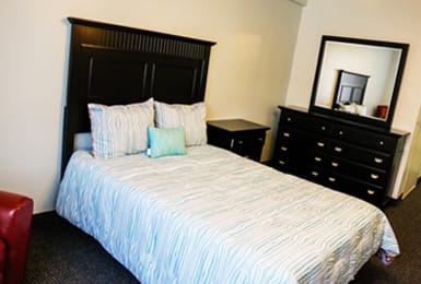 A neatly arranged bedroom featuring a bed with pillows, a nightstand, and a dresser with a mirror.