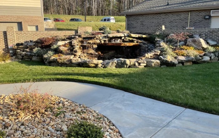 A landscaped garden area with a pond and rock formation, bordered by a curved pathway.