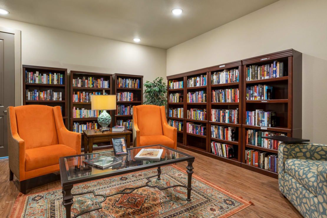 Cozy library with orange armchairs, bookshelves, and a decorative rug.