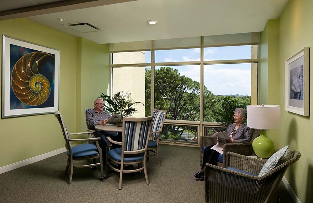 Elderly individuals relaxing in a comfortable seating area with a scenic window view.
