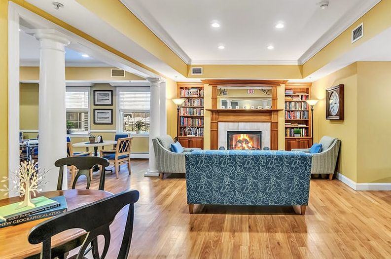 A cozy living room with a fireplace and bookshelves, featuring a blue sofa and warm lighting.