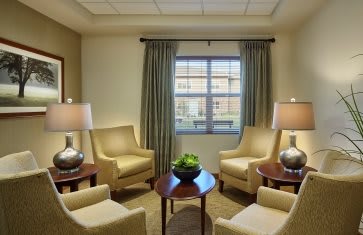 A cozy living room with comfortable chairs, elegant lamps, and a central table near a window.