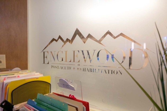 An office reception area with a logo etched on a glass wall and colorful folders on a desk.