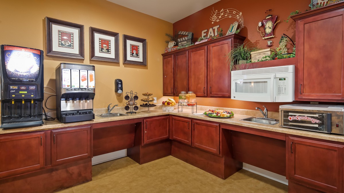 A cozy kitchen corner featuring a breakfast area with a beverage dispenser and microwave, surrounded by warm wooden cabinets and decorative elements.