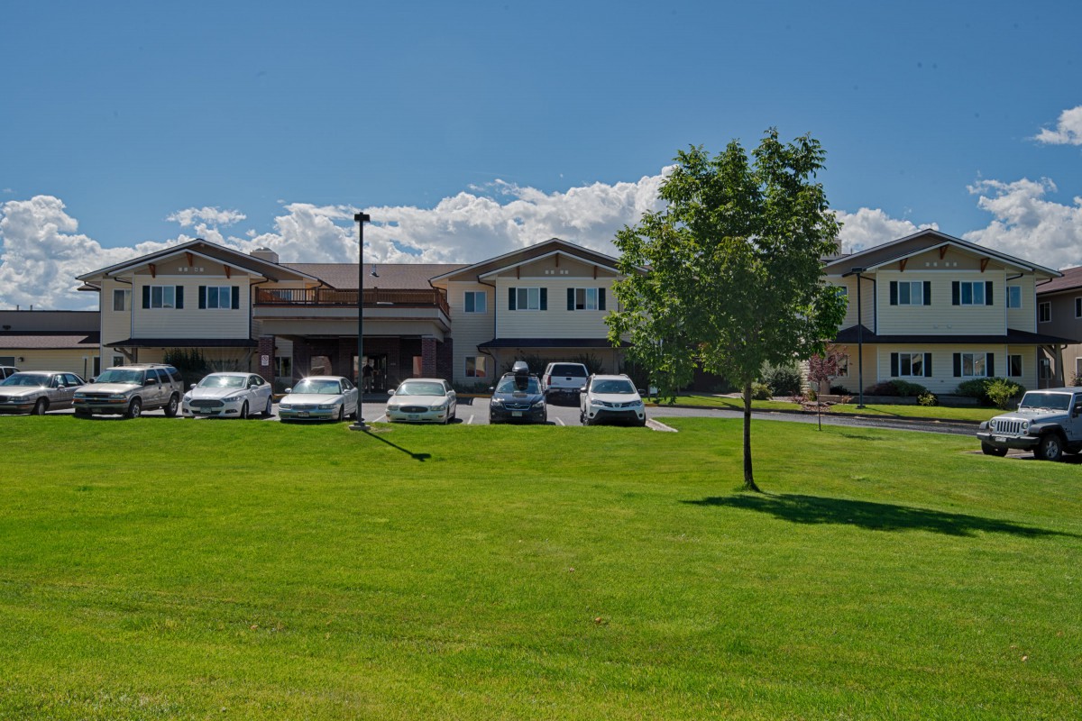 A building with a parking lot in front, surrounded by a grassy area and trees under a clear blue sky.