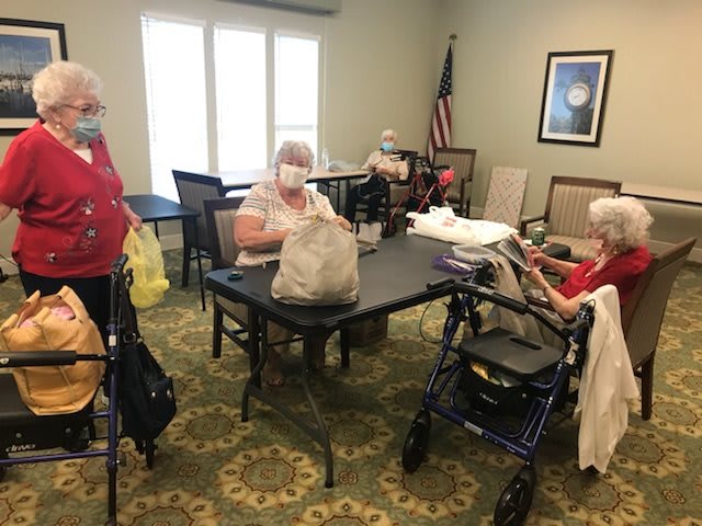 A group of seniors socializing around a table in a community room, wearing masks.