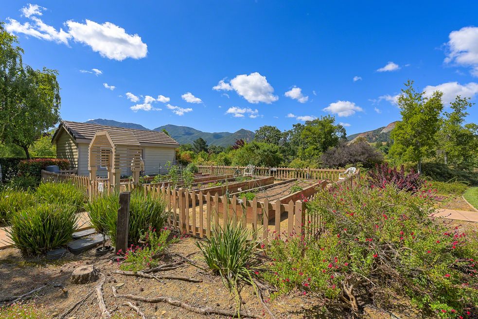A tranquil garden surrounded by a wooden fence, set against a backdrop of mountains and a clear blue sky.