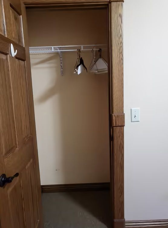 An empty closet with a few hangers inside, viewed through an open wooden door.