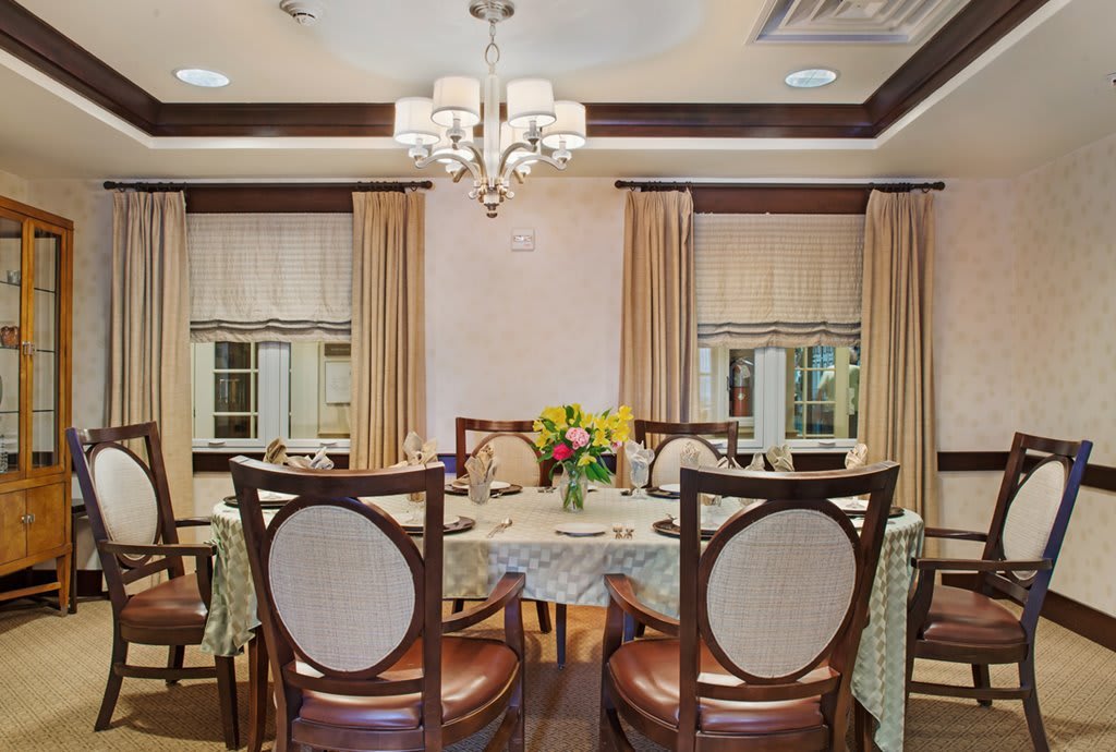 A luxurious dining room featuring an elegant table setting with a chandelier above and decorative curtains framing the windows.