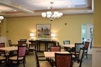 A cozy dining room with neatly arranged tables and chairs, featuring a chandelier and decorative painting on the wall.