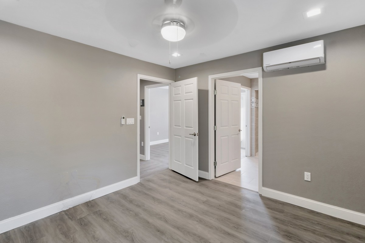 A modern empty room with gray walls, laminate flooring, and a ceiling fan.