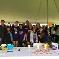 A group of people gathered under a tent at an event, standing behind a table filled with candy.