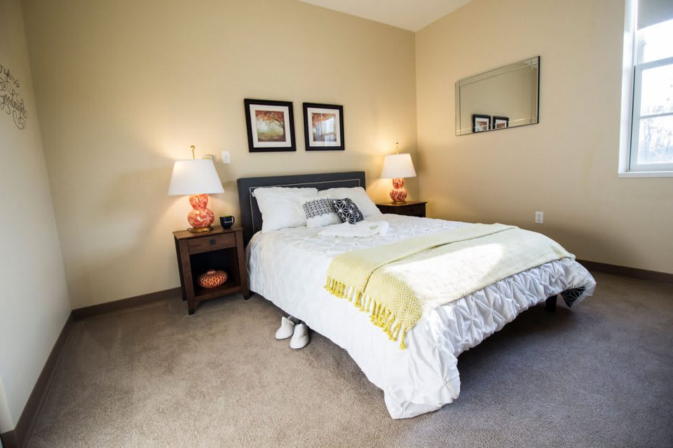 A cozy bedroom with a neatly made bed, two lamps on nightstands, and framed pictures on the wall.