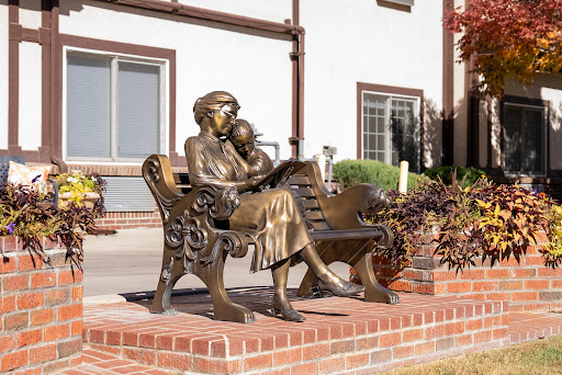 A beautiful bronze statue depicting a mother reading to her child, seated on a decorative bench.