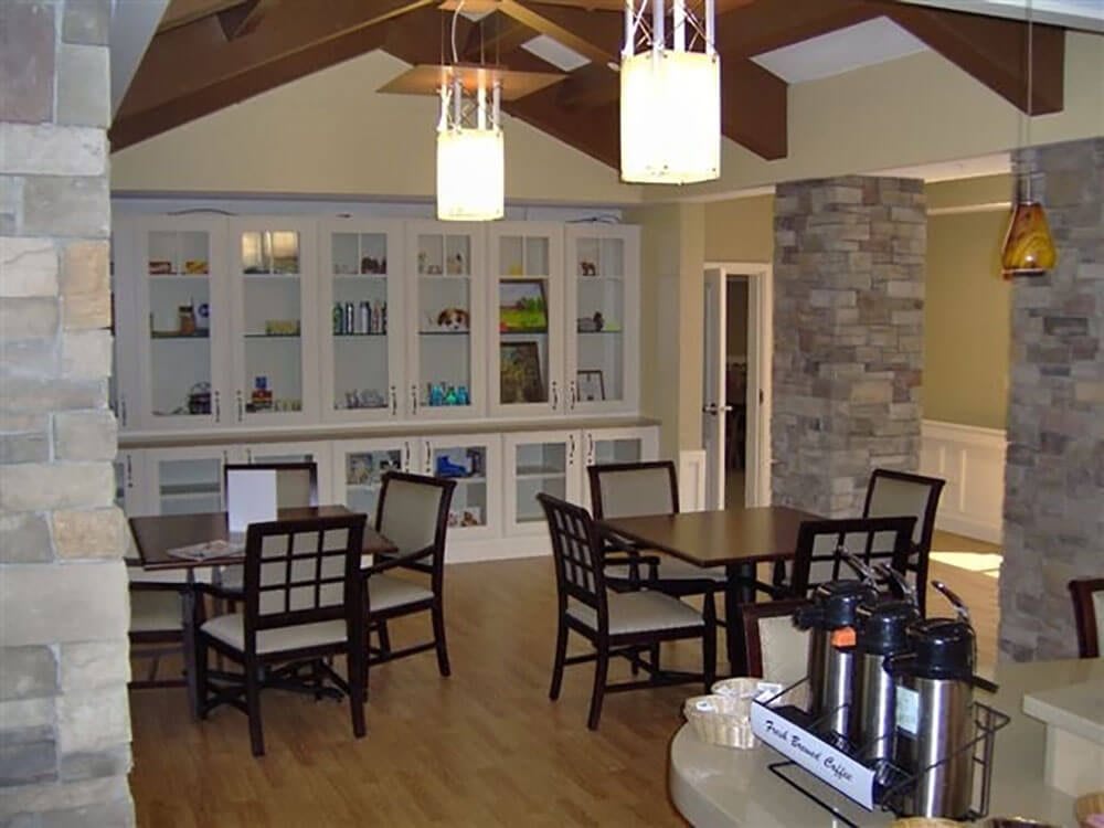 A cozy dining area with wooden floors, tables, and chairs, featuring elegant lighting and a stone column.