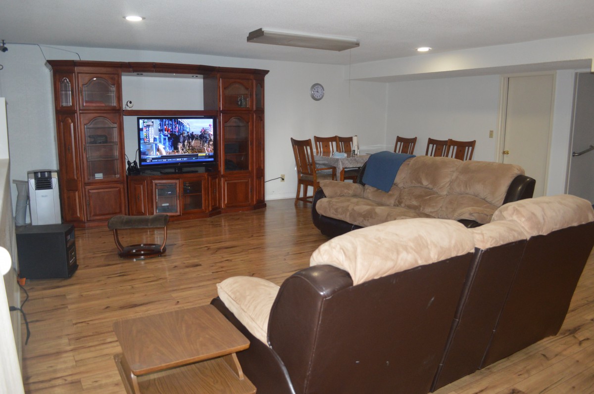 A spacious living room featuring a comfortable sofa, a TV set in a wooden entertainment center, and a dining area with a table and chairs.