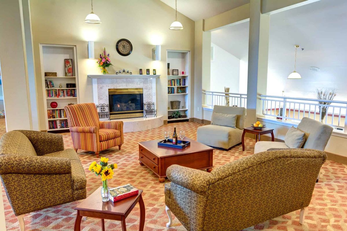 A cozy living room with comfortable armchairs, a fireplace, and shelves filled with books.