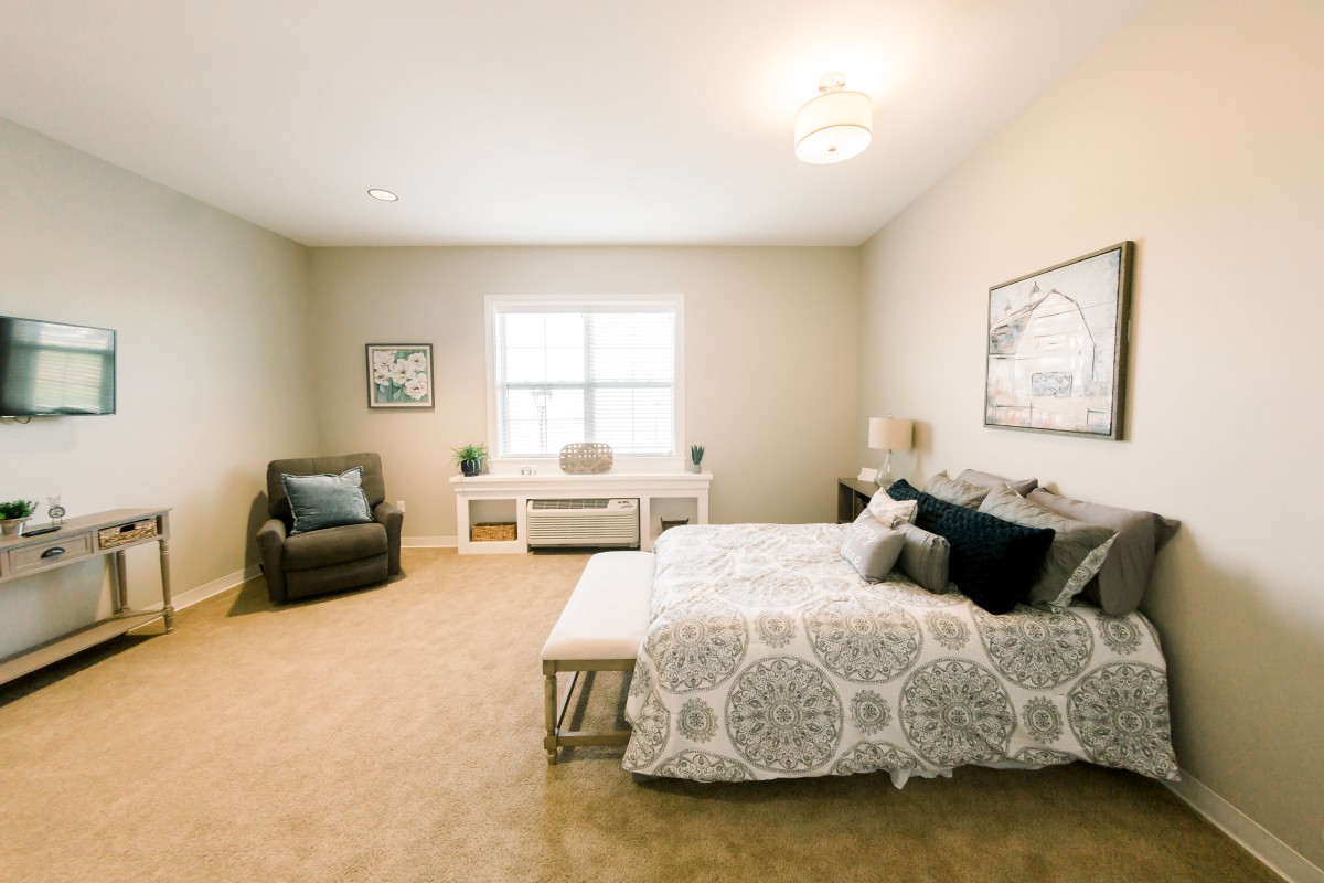 A cozy and spacious bedroom with modern decor, featuring a bed, armchair, and simple artwork.