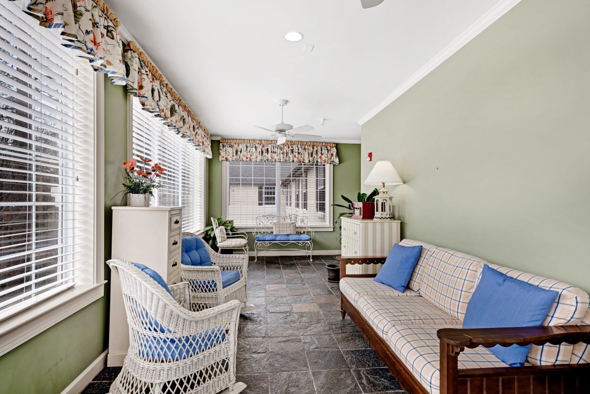 A cozy living room with wicker furniture, green walls, and ample natural light.
