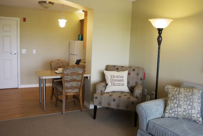 A cozy living room with an armchair and a floor lamp, adjacent to a dining area.