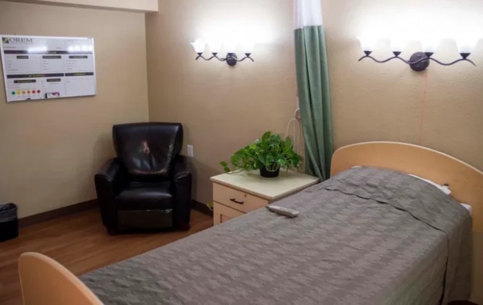 A cozy bedroom with a bed, leather chair, and a nightstand adorned with a plant.