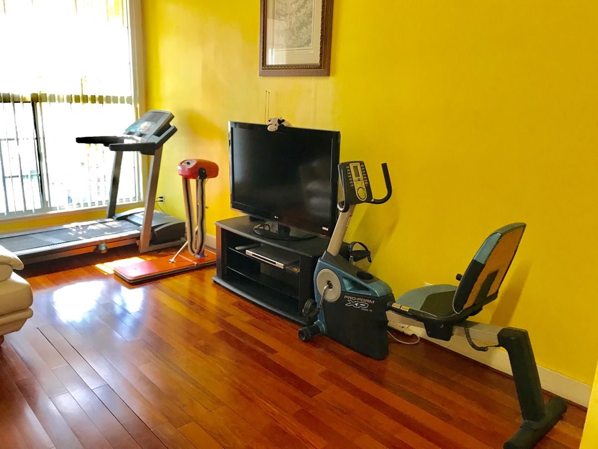 A home gym setup featuring a treadmill, stationary bike, and a television on wooden flooring with yellow walls.
