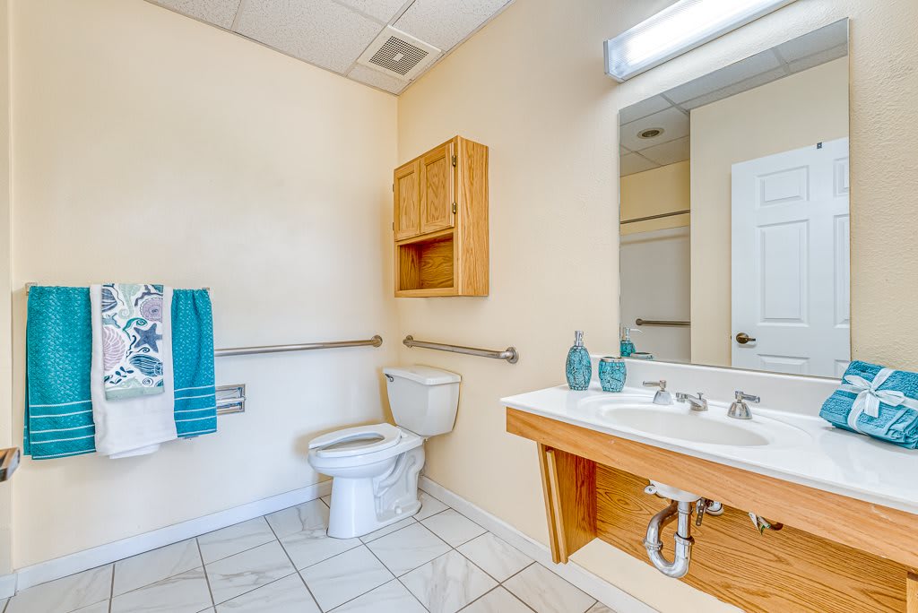 A clean and accessible bathroom with a toilet, sink, and mirror.