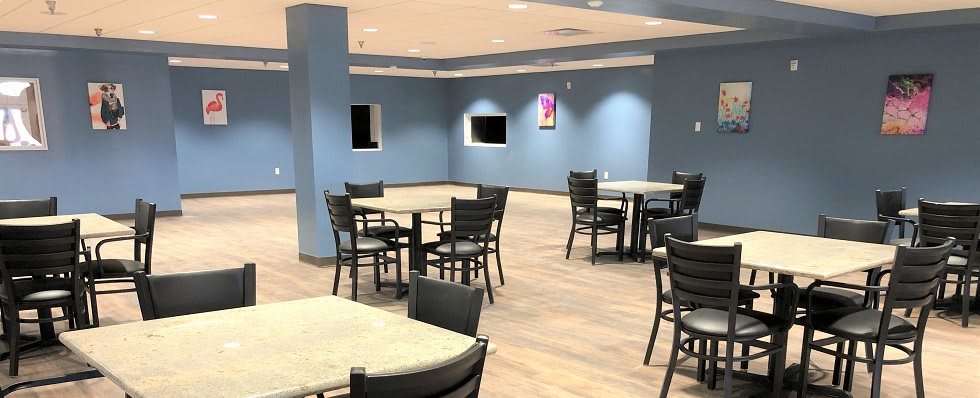 An empty cafeteria with blue walls, featuring several tables and chairs.