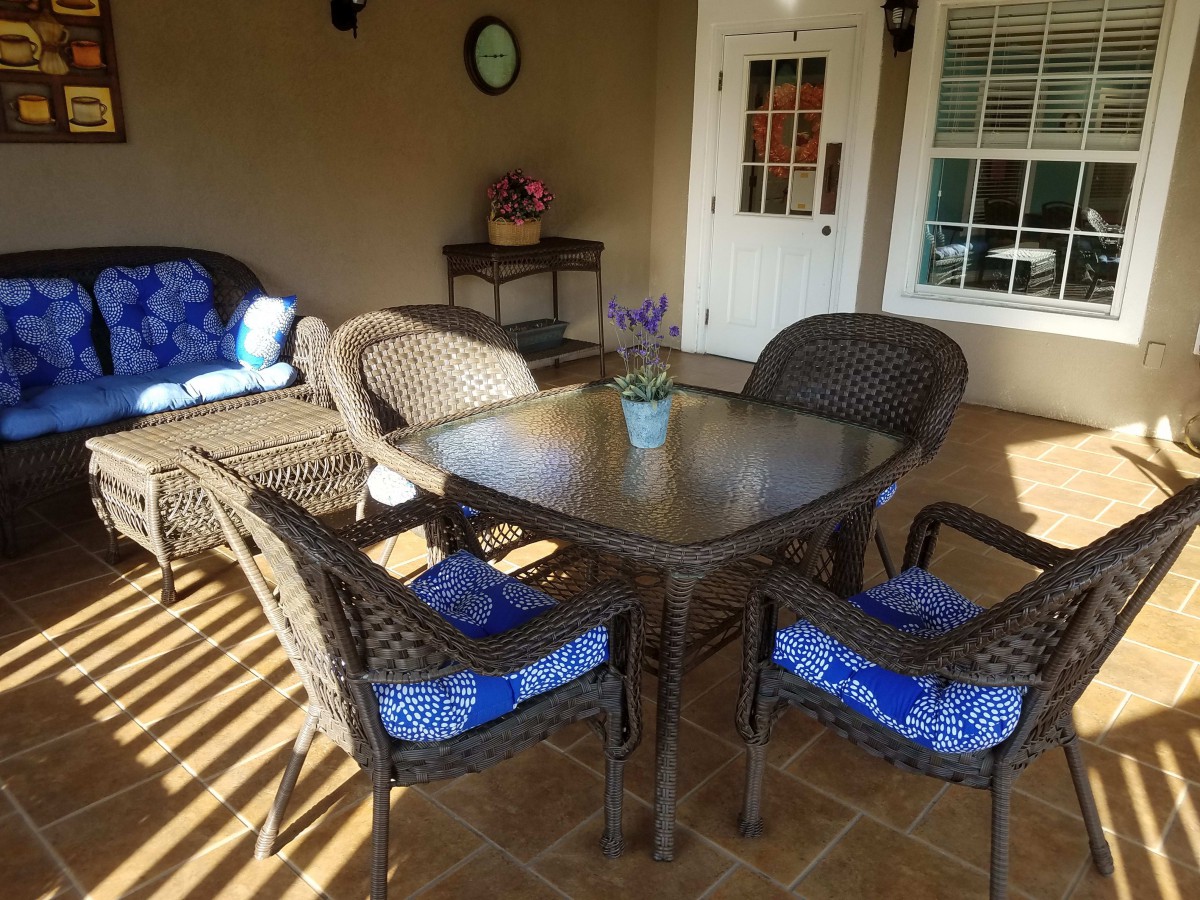 An inviting patio setup with wicker furniture and blue cushions, bathed in sunlight.