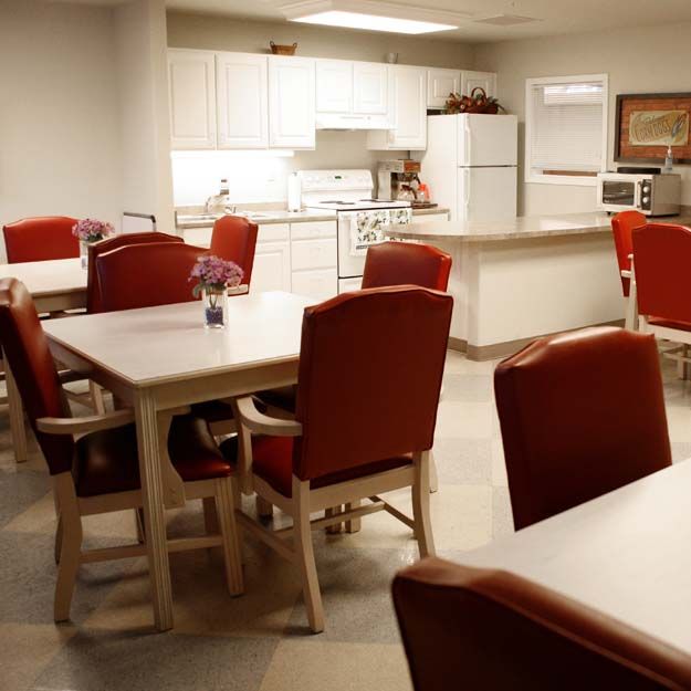 A cozy kitchen and dining area with red chairs and white tables.