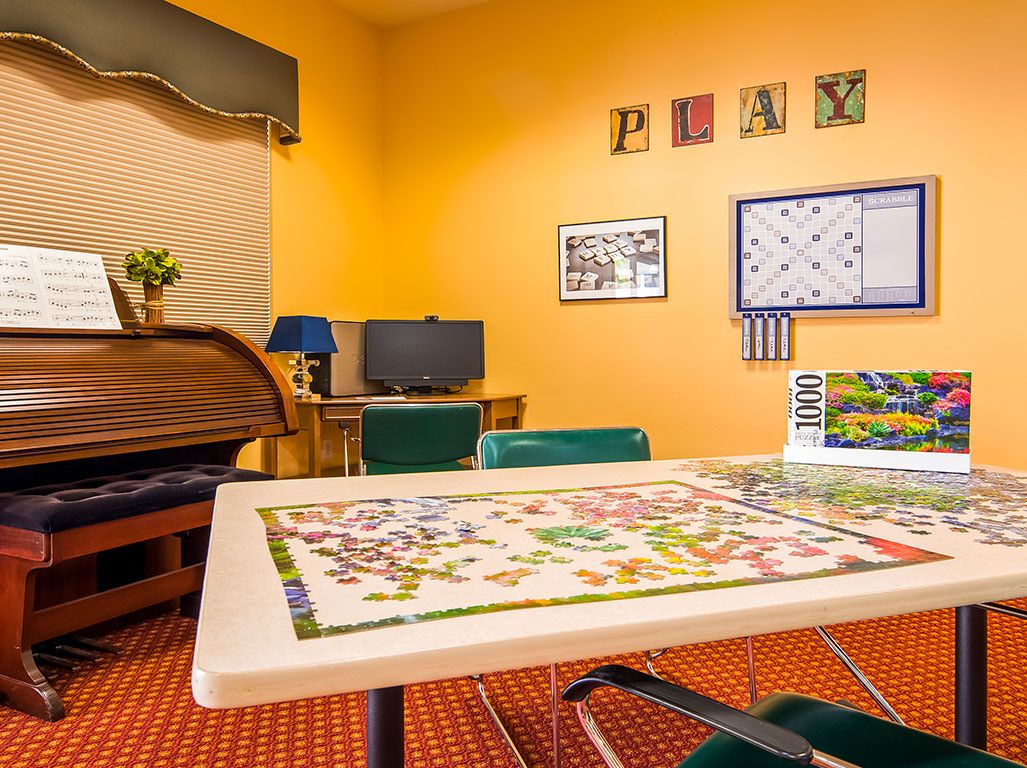 A cozy game room featuring a table with a board game and puzzle, surrounded by chairs, and decorated with playful wall art.