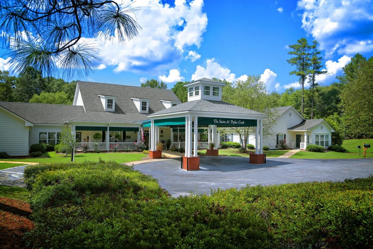 A picturesque building with a covered entrance surrounded by greenery and a blue sky with clouds.