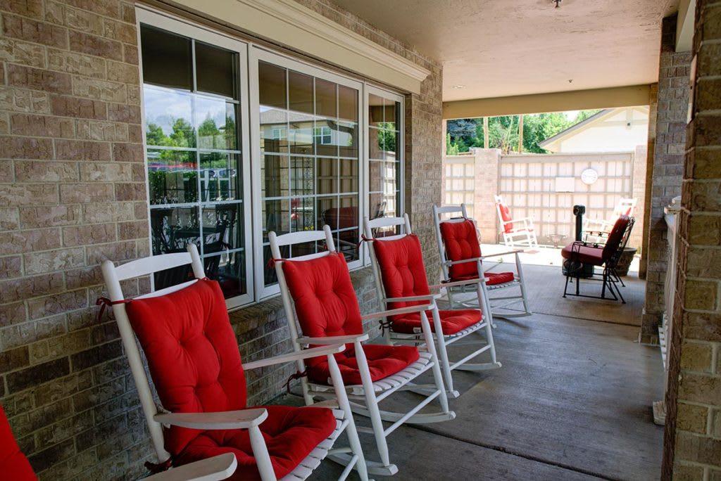 A cozy covered patio with white rocking chairs featuring red cushions, perfect for relaxation.