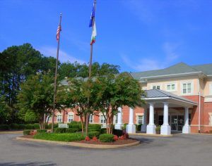 A building with flags and a landscaped entrance featuring columns.