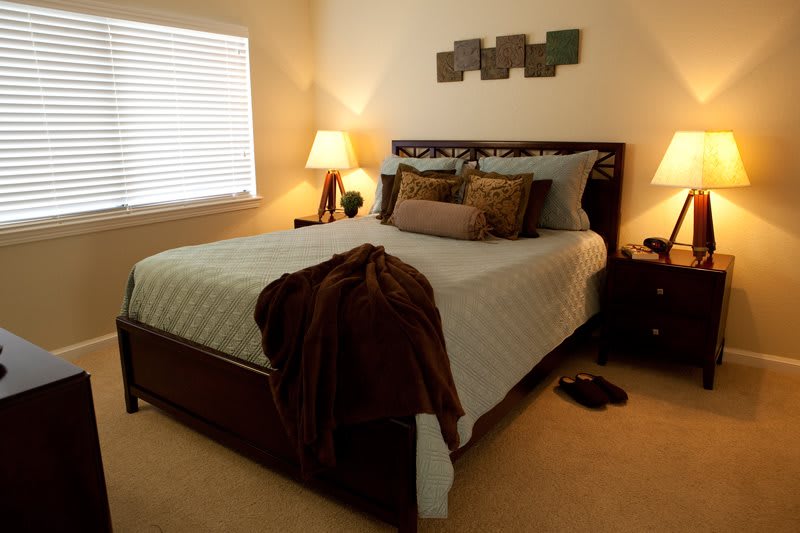 A cozy bedroom with a neatly made bed, soft lighting from lamps, and decorative pillows.