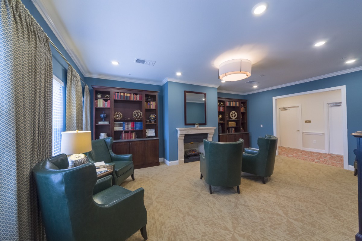 A cozy living room with blue walls, featuring bookshelves, armchairs, and a fireplace.
